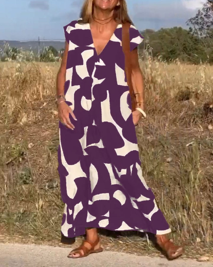 Front view of a model in a purple and white abstract print vintage long dress with a brown leather tote bag