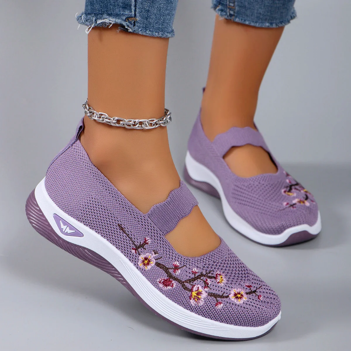 Side view of model wearing purple breathable slip-on sneakers with pink floral embroidery and an ankle bracelet