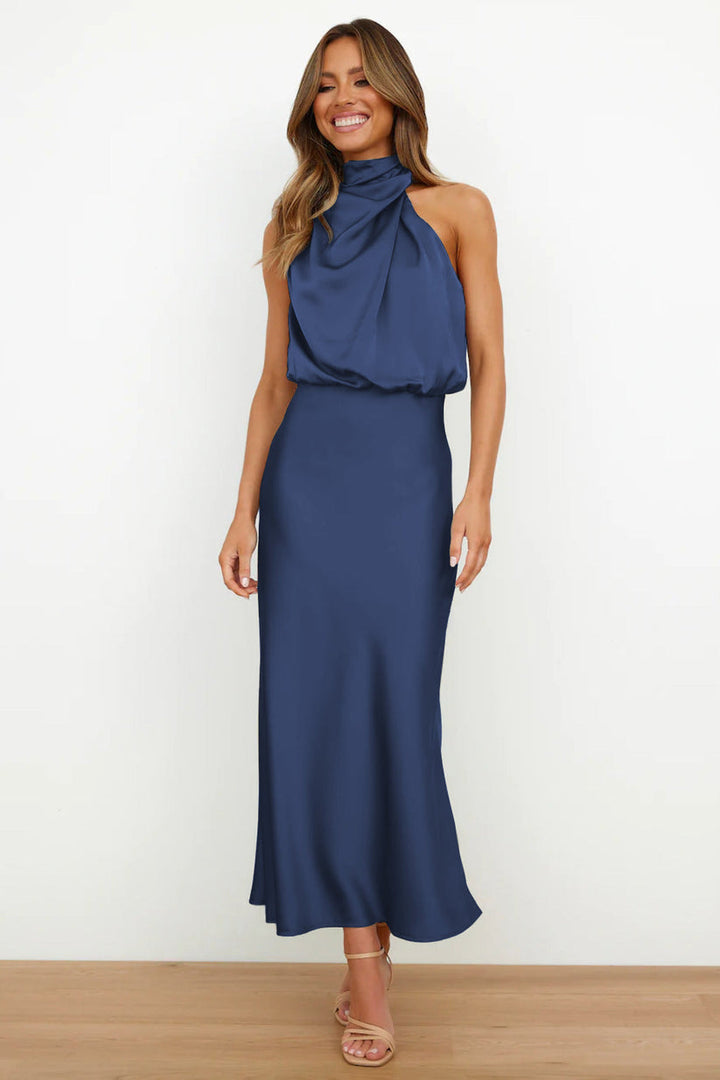Front view, model wearing a long satin dress in navy with a draped halter neckline and flowing skirt