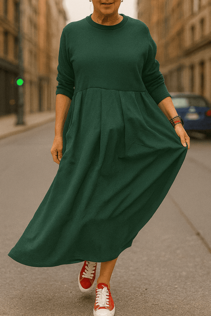 Front view, model wearing a dark green oversized long sleeve dress with a round neck, pockets and a pleated skirt