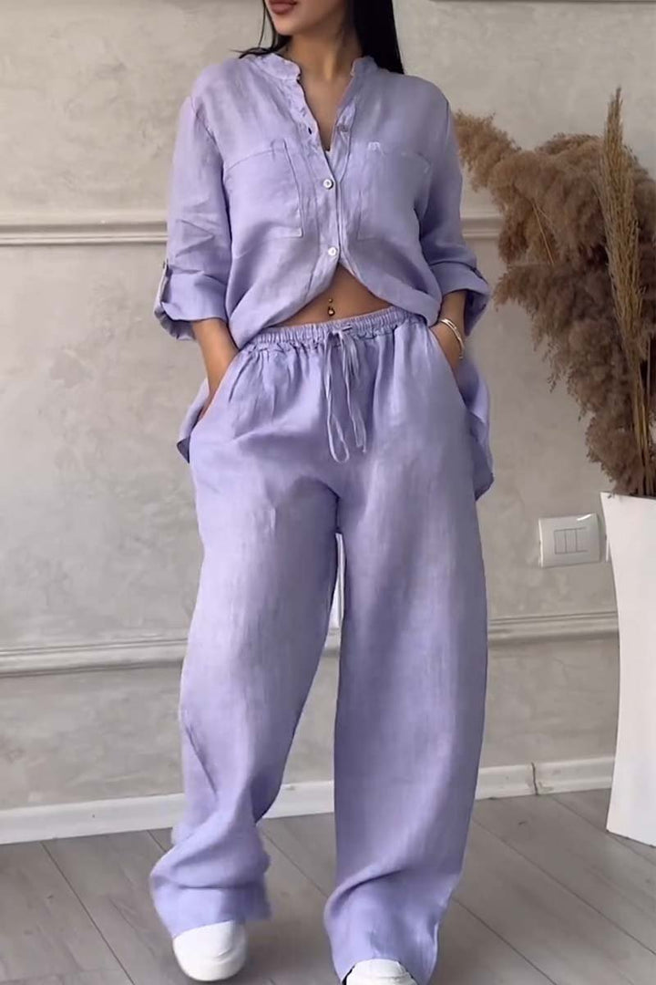 Front view of a model in a lilac long sleeve blouse and wide leg pants set with hands in pockets
