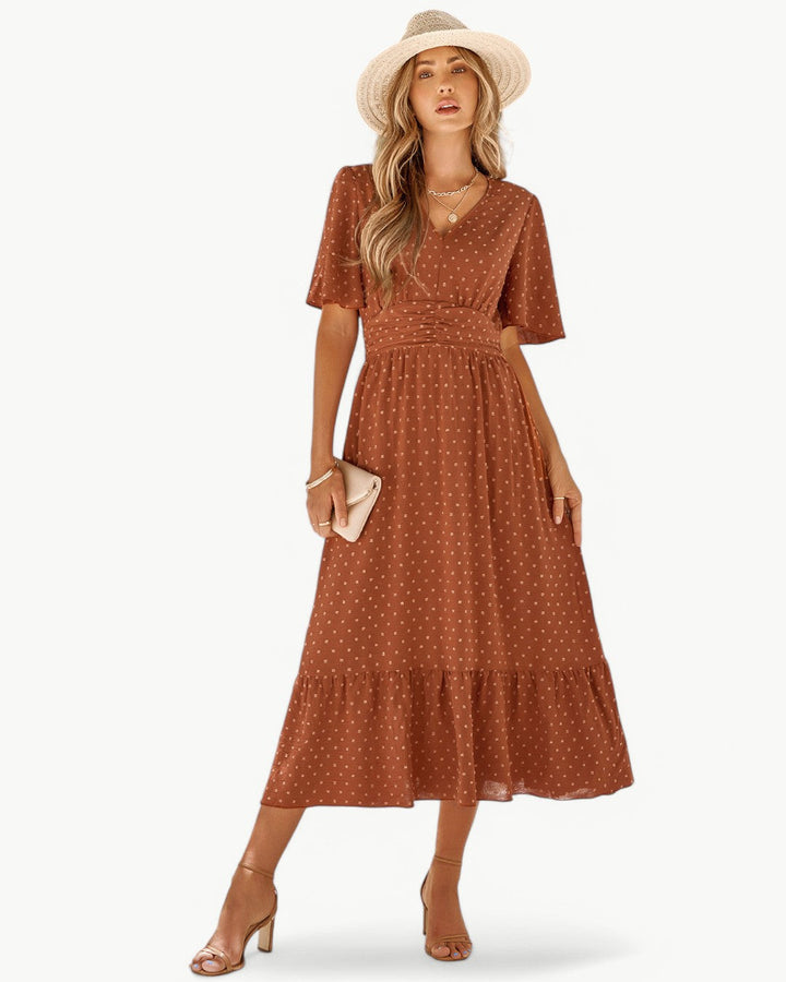 Front view, worn by model, a V-neck maxi dress with short sleeves in rust with white polka dots and a straw hat