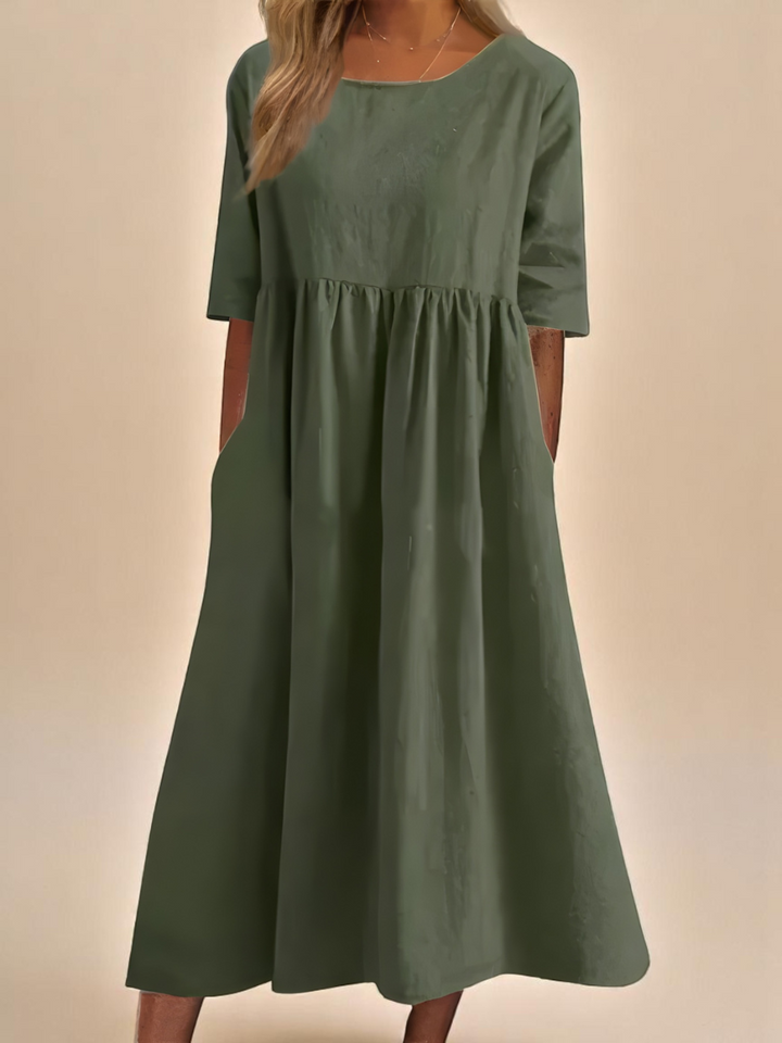 Front view of a model wearing a dark green soft cotton airy dress with three quarter sleeves and side pockets