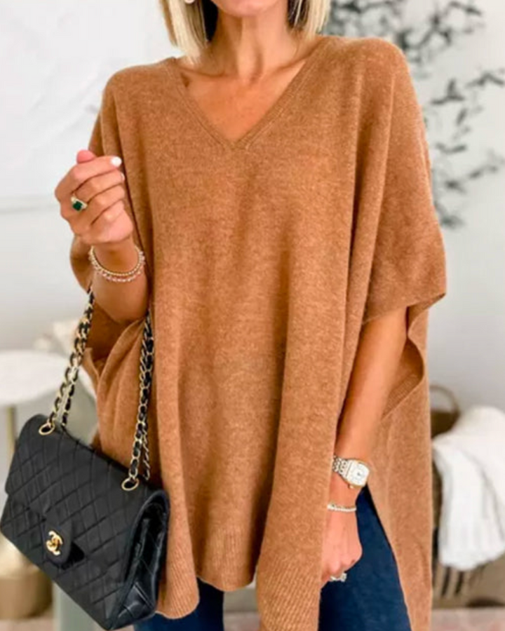 Front view of model wearing the Erica oversized V-neck poncho sweater in a warm brown, holding a black handbag