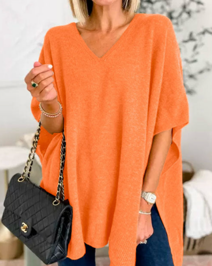 Front view of model wearing the Erica oversized V-neck poncho sweater in a vibrant orange, holding a black handbag