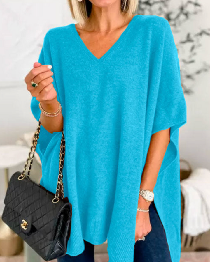 Front view of model wearing the Erica oversized V-neck poncho sweater in bright blue, holding a black quilted handbag