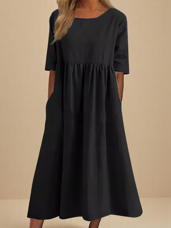 Front view of a model wearing a dark grey soft cotton airy dress with three quarter sleeves and hands in pockets