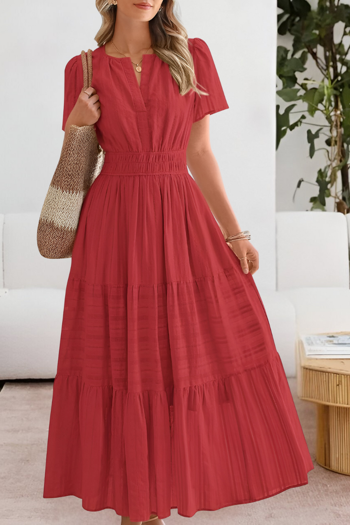 Front view of a woman in a red Boho Breeze summer dress with a smocked waist, holding a striped bag