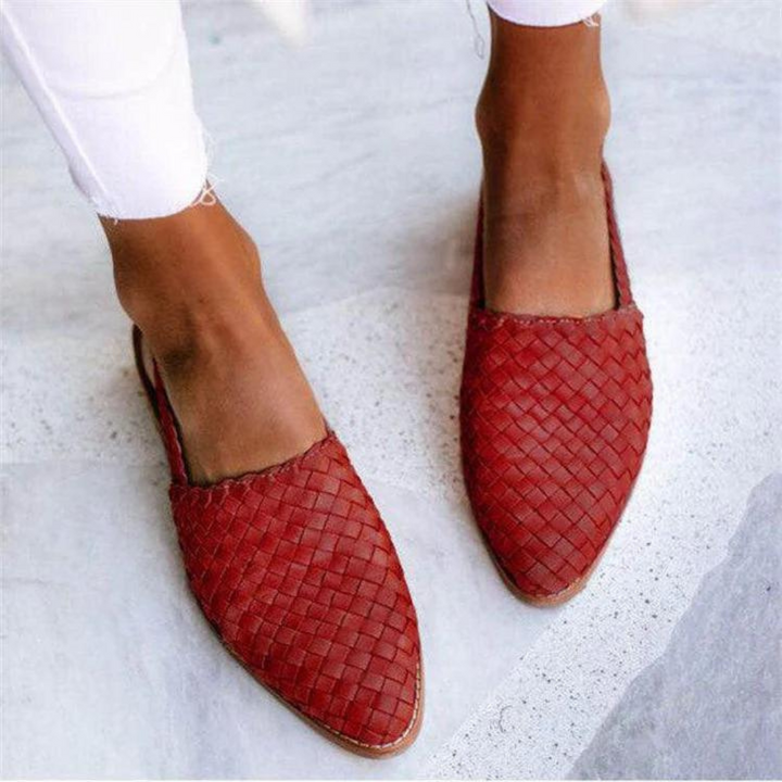 Top view of two feet in red woven flat sandals, worn by model with white pants