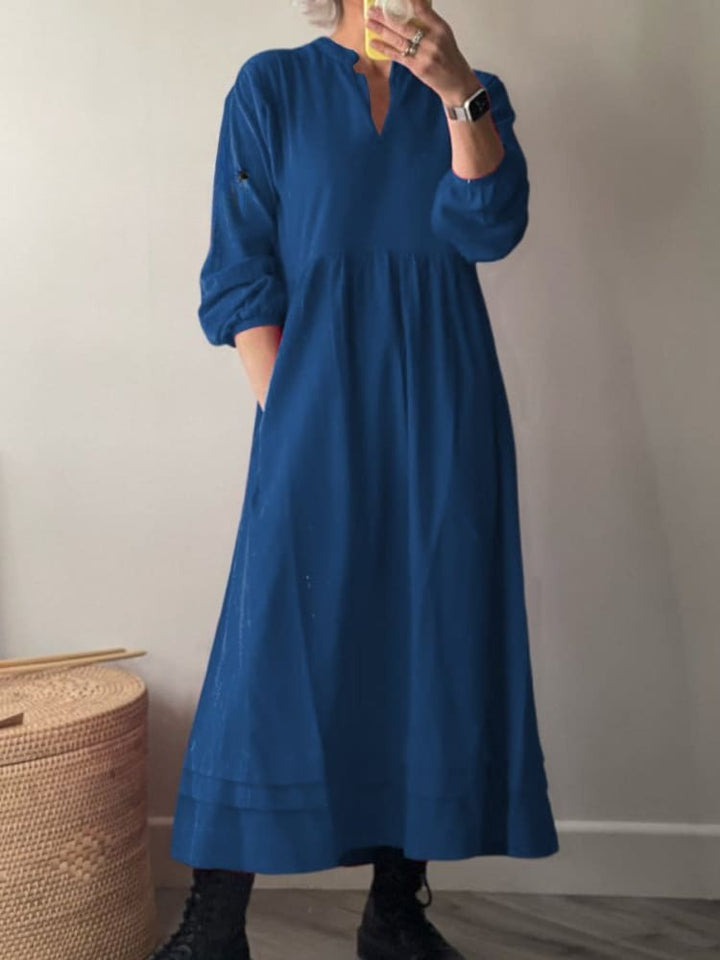 Front view, model wearing a blue cotton dress with pockets, long sleeves, and a v-neckline
