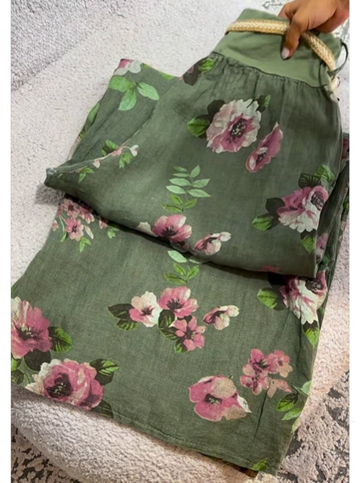 Flat lay of floral print cotton linen pants with a hand holding the braided drawstring waist