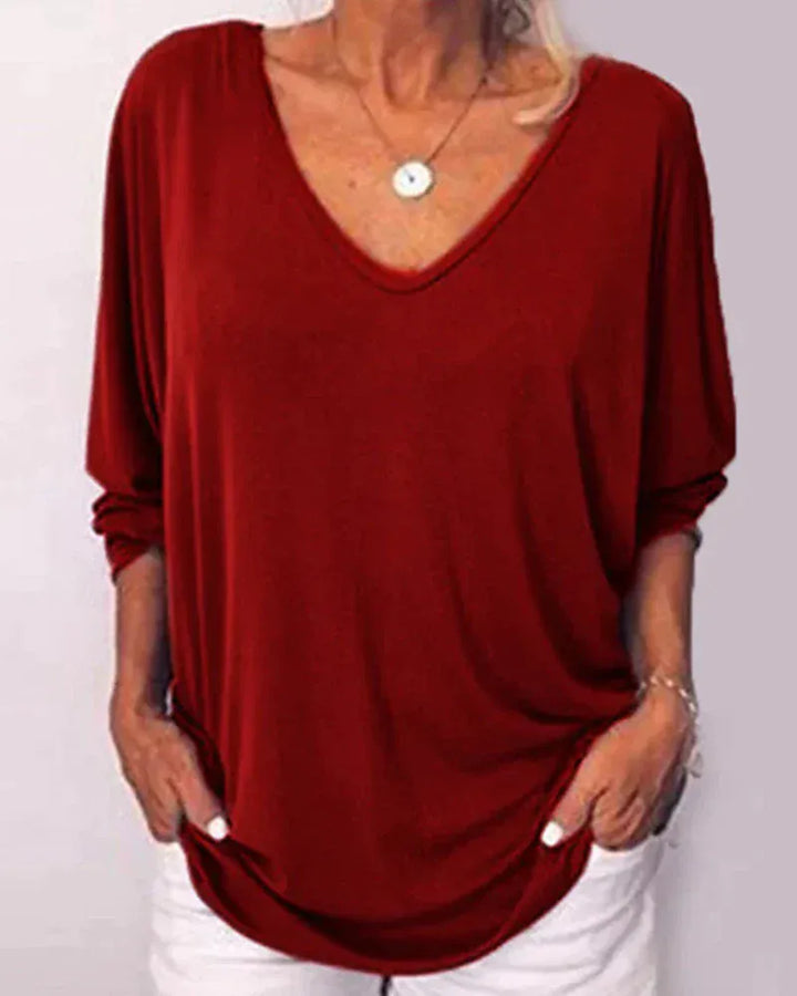 Front view of a model wearing a loose-fitting linen V-neck blouse in a rich red with 3/4 sleeves and a pendant