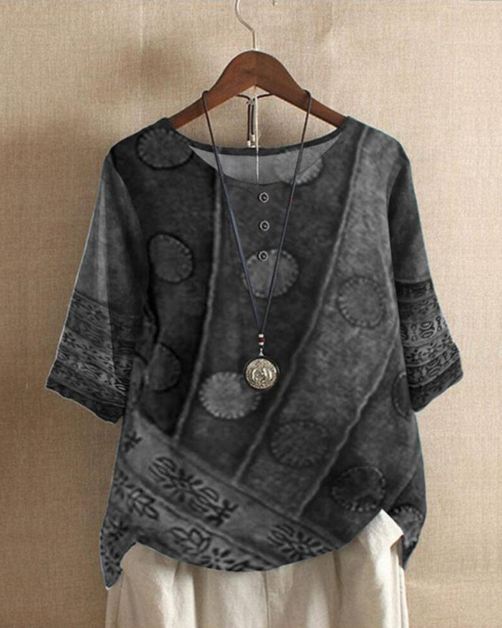Front view of a Lacey Casual Blouse in a dark digital print, with a necklace and light coloured pants