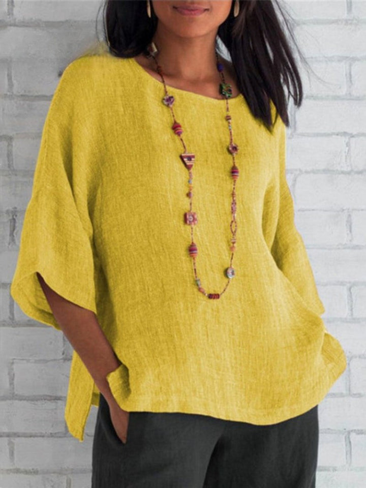 Front view of a model wearing a yellow crewneck cotton linen shirt top with a long beaded necklace