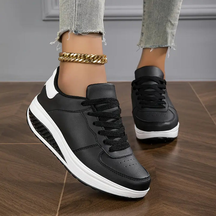 Close up, worn by model, of black Myrtle comfort sneakers with thick white soles and a gold ankle bracelet