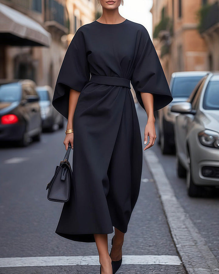 Front view of a model in a black kimono sleeve midi dress with an elegant self-tie belt and a black handbag