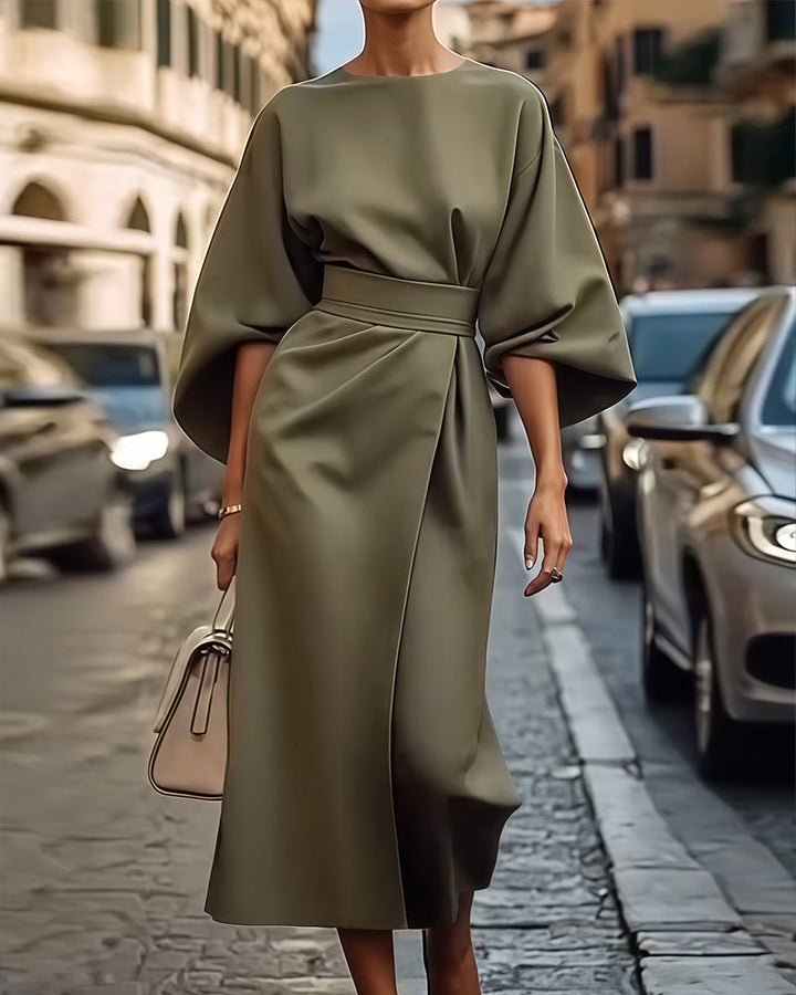 Front view of a model in an elegant belted kimono sleeve midi dress with a light handbag on a street