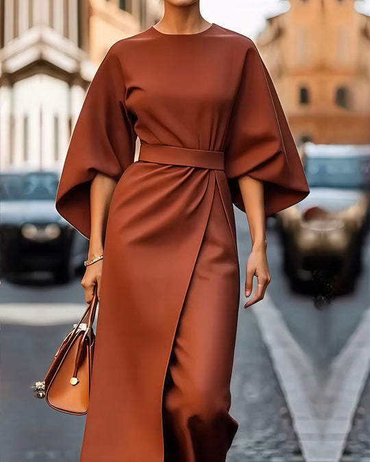 Front view of a model in an elegant belted kimono sleeve midi dress with a brown handbag on a street, alternate angle