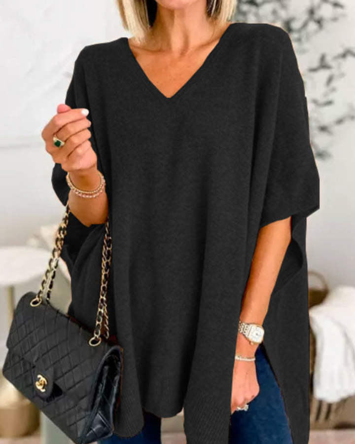 Front view of model wearing the Erica oversized V-neck poncho sweater in black, holding a quilted black handbag