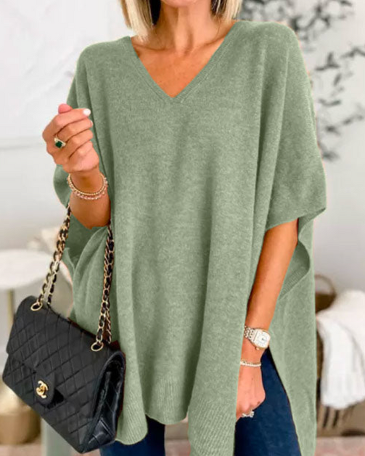 Front view of model wearing the Erica oversized V-neck poncho sweater in sage green, holding a black handbag