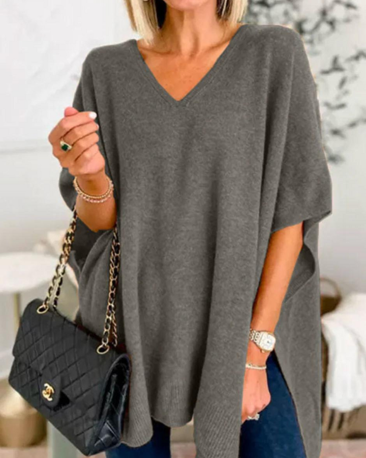 Front view of model wearing the Erica oversized V-neck poncho sweater in dark grey, holding a black quilted handbag