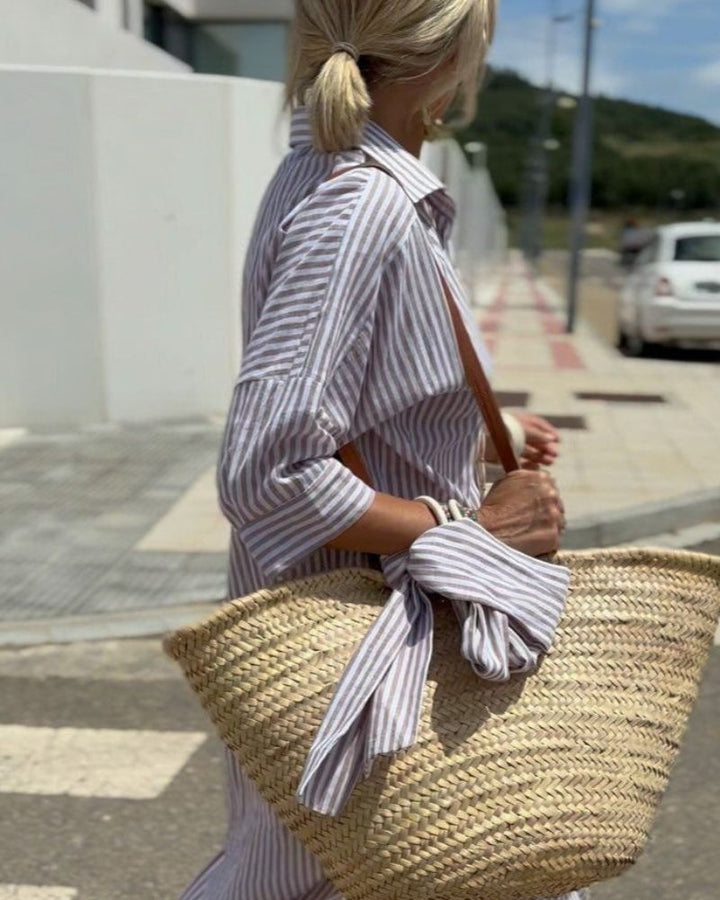 Back view of the Classic Striped Lace-Up Shirt Dress worn by model with a straw bag and a matching striped scarf