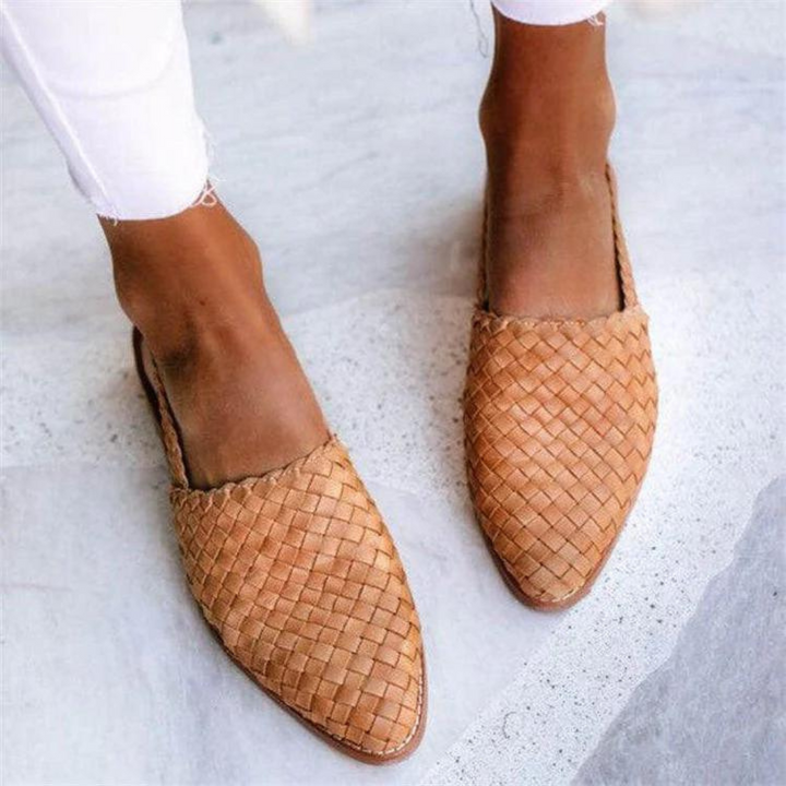 Top view of two feet in tan woven flat sandals, worn by model with white pants