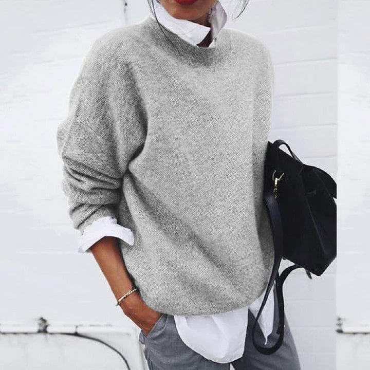 Front view of a model wearing a light grey oversized knit jumper over a white shirt with grey pants