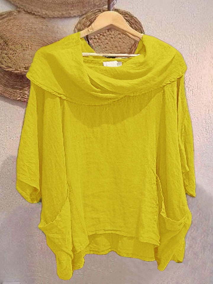 Front view of a yellow linen pocket top with a draped neck and 3/4 sleeves, held on a wooden hanger
