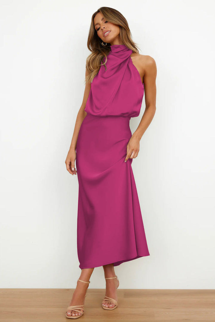 Front view, model wearing a long satin dress in vibrant magenta with a draped halter neckline and flowing skirt