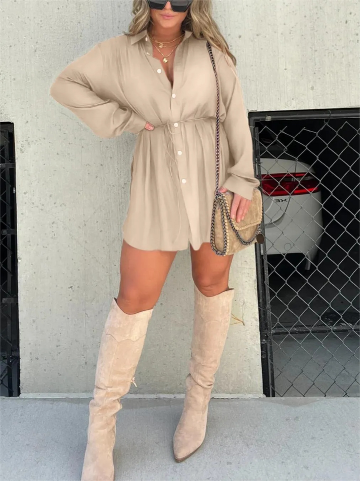 Front view, model wearing a beige satin romper with a self-tie belt and beige knee high boots