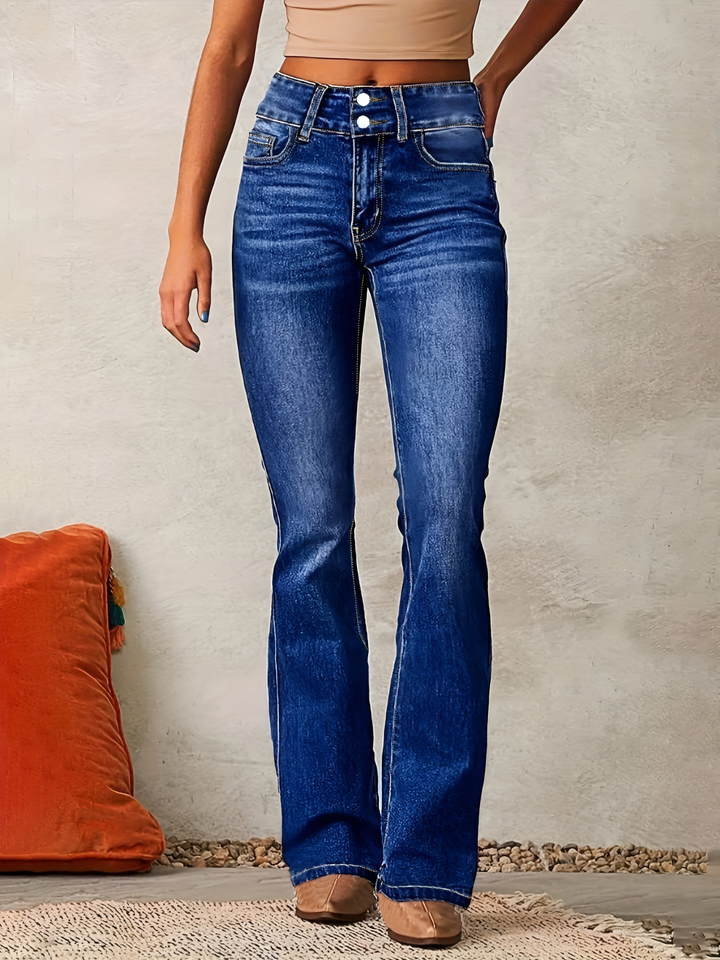 Front view of a model wearing high-waisted flared jeans in vintage blue denim with a light crop top and orange cushion