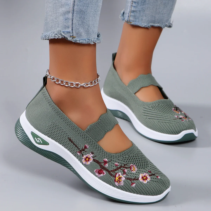 Close up of model wearing green breathable slip-on sneakers with pink floral embroidery and an ankle bracelet
