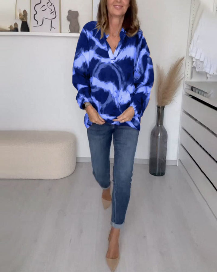 Front view of a woman walking in a casual printed V-neck blouse, untucked, with cuffed blue jeans and nude heels
