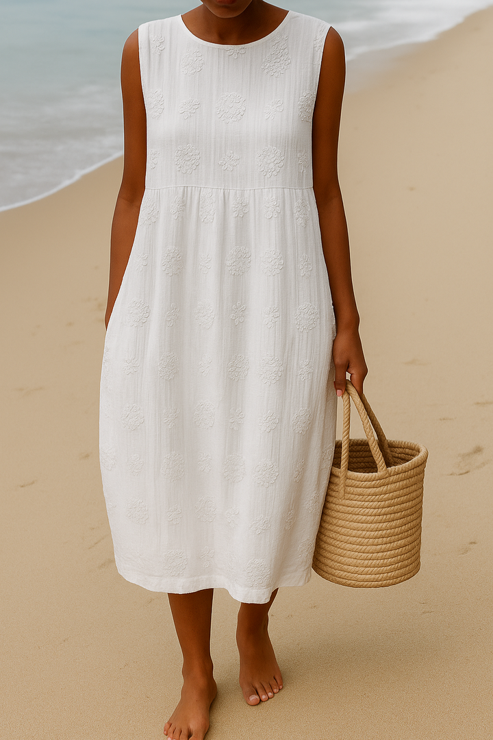 Front view of a model wearing the white sleeveless A-line boho dress with floral embroidery and a basket on the beach