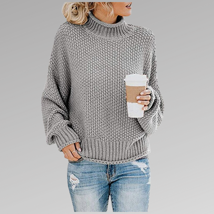 Front view of a model wearing the grey Jovana Airy Touch Knit top with ripped jeans and holding a coffee cup