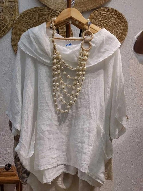 Front view of a white linen pocket top with a draped neck and 3/4 sleeves, adorned with a pearl necklace