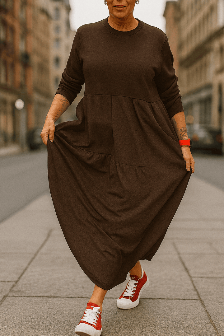 Front view, model wearing a brown oversized long sleeve dress with a round neck, pockets and a tiered skirt