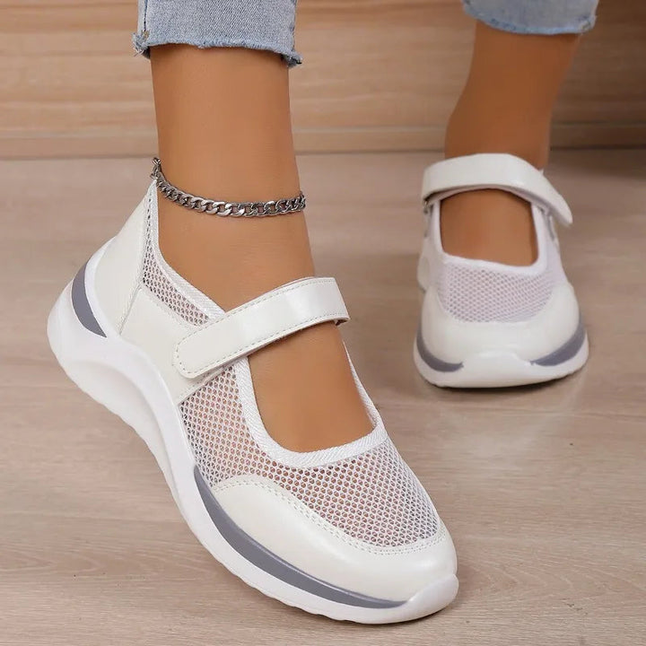 Back view of white orthopedic Mary Jane shoes with mesh and grey accents on a model wearing an anklet