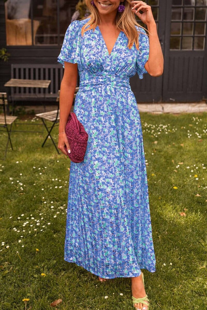 Three quarter view of the Elegant V-Neck Maxi Dress, a blue floral dress on a model holding a pink clutch