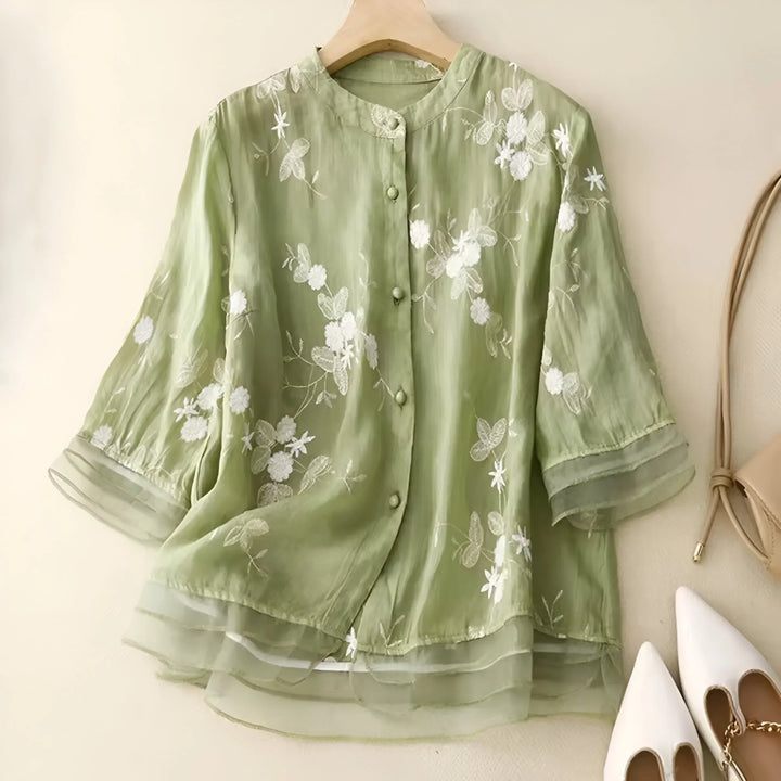 Front view of a green lightweight cotton blouse with white floral embroidery, sheer layered sleeves and hem