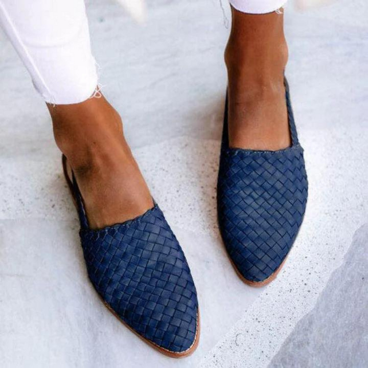 Top view of two feet in navy woven flat sandals, worn by model with white pants