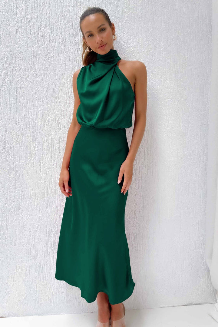 Front view, model wearing a long satin dress in emerald green with a draped halter neckline and flowing skirt