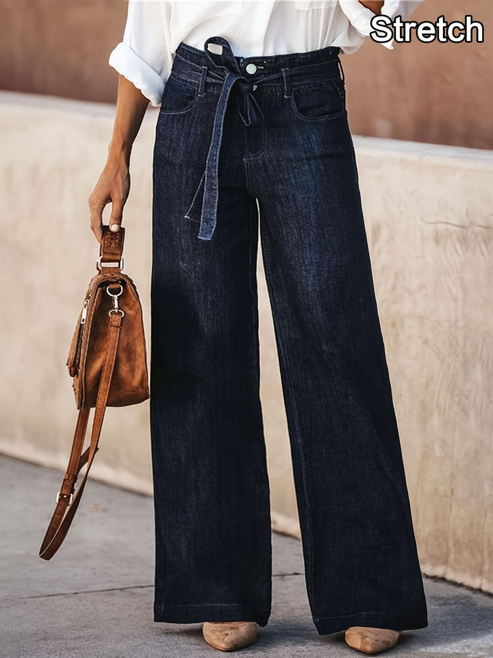 Front view, worn by model, of dark wash wide leg jeans with a denim tie belt, holding a brown handbag