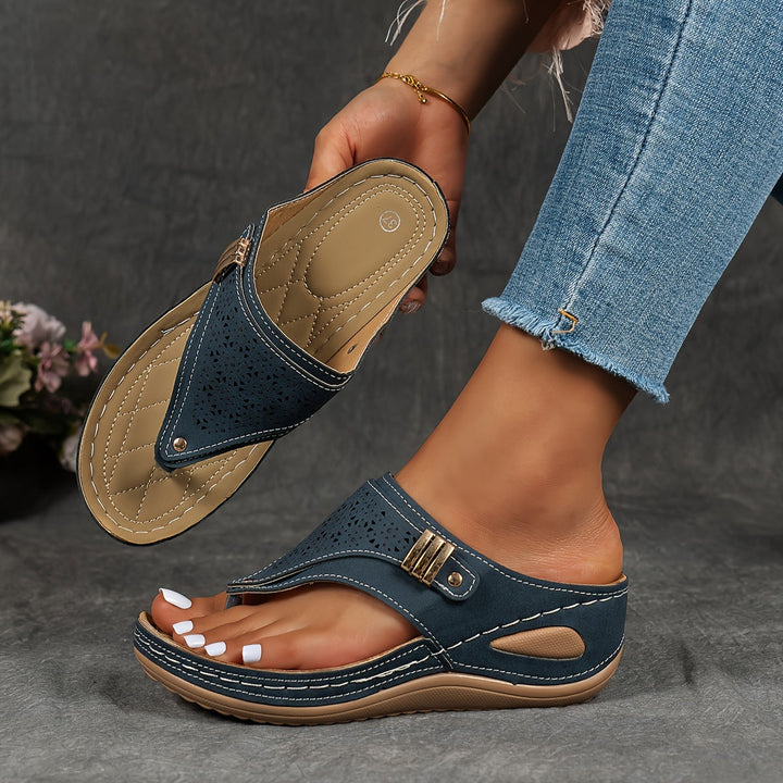 Close up of a model wearing one blue orthopedic leather sandal, holding another to show arch support comfort