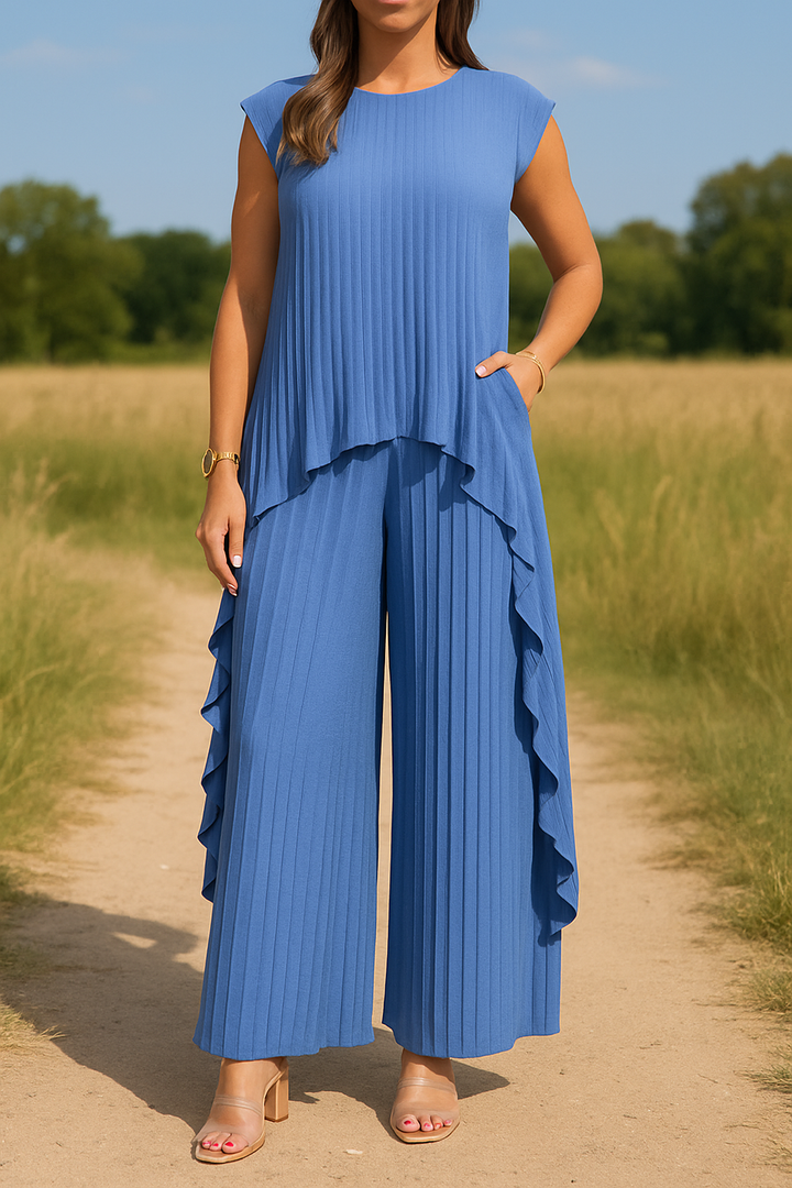 Front view of a woman in a blue irregular pleated top wide leg pants set, with one hand in her pocket