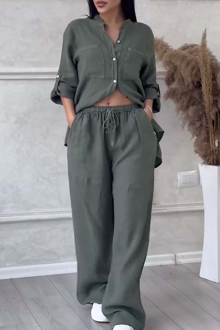 Front view of a model in an olive green long sleeve blouse and wide leg pants set with hands in pockets