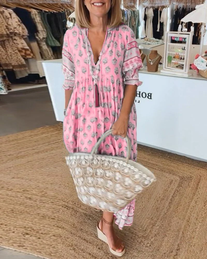 Front view of a woman wearing a pink casual V-neck dress with a grey print and a woven tote bag