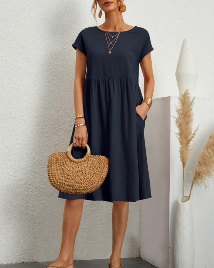 Navy blue short sleeve summer dress, worn by model, front view, with pockets and a straw handbag