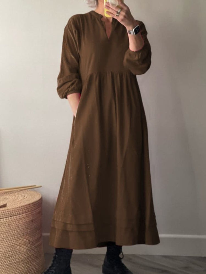 Front view, model wearing a brown cotton dress with pockets, long sleeves, and a v-neckline